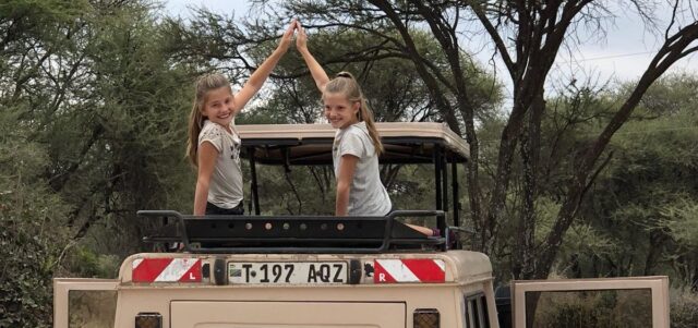 twee lachende jonge kinderen met high five zitten op het dak van de safari auto safari met jonge kinderen