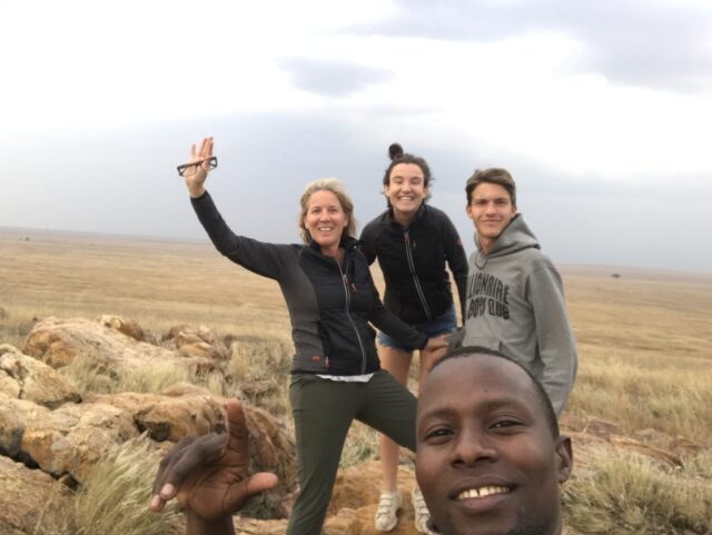 zwaaiende moeder met oudere meisje en jongen met op de voorgrond de gids op de vlaktes van de serengeti tanzania