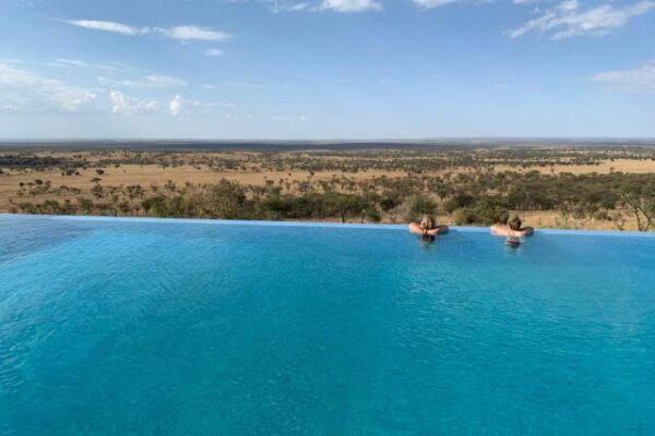 infinity pool zwembad met twee mensen erin uitkijkend over de serengeti vlakte kubu kubu tanzania