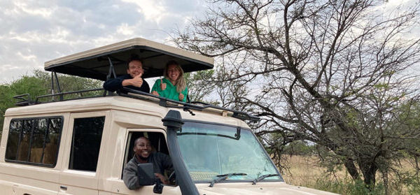 Net getrouwd stel staand in de safari auto met dak omhoog en gids achter het stuur tijdens huwelijksreis door tanzania